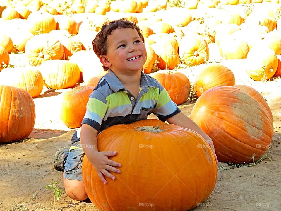 Smiling boy sitting near pumpkin
