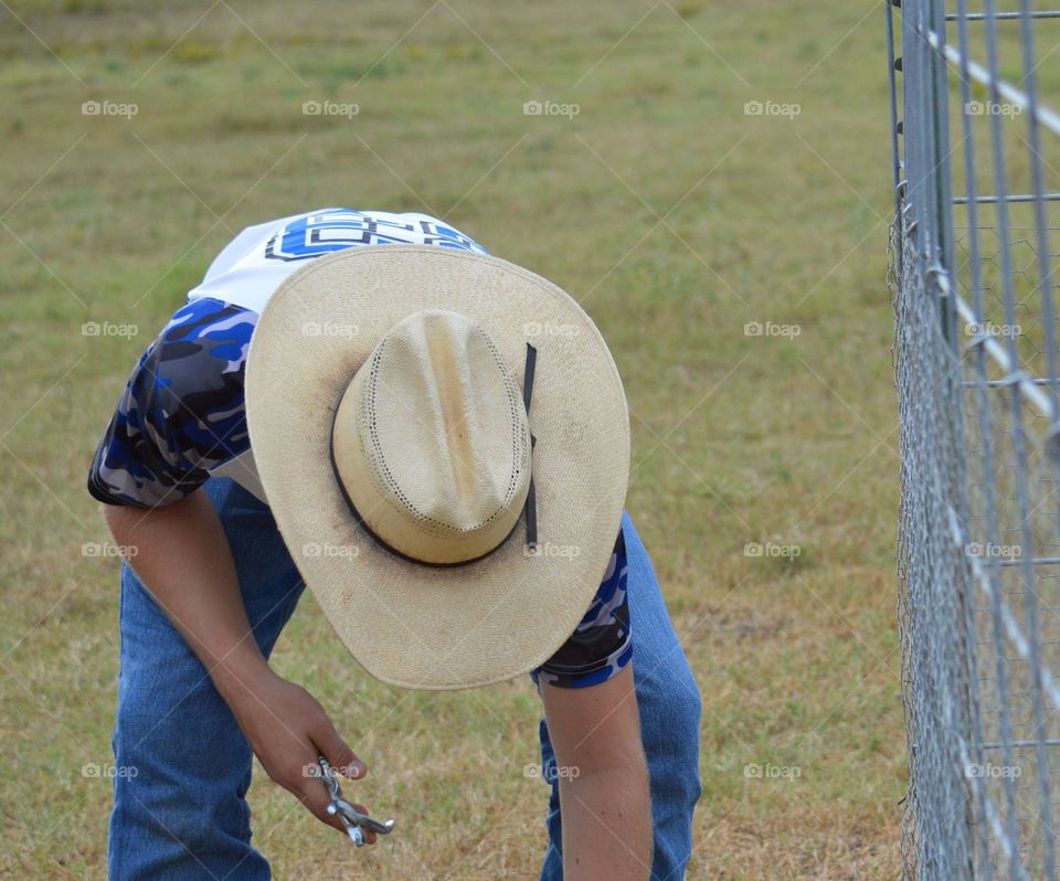 Young cowboy building  fence by hand. 
