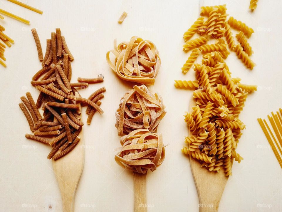 wooden ladles containing different types of pasta photographed from above