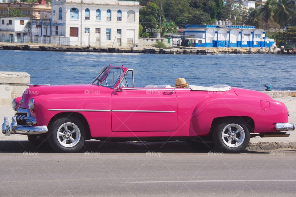 A classic American pink convertible car parked on the famous Malecon Avenue in Havana, Cuba