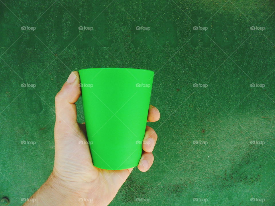 Hand holds a green glass on a green background