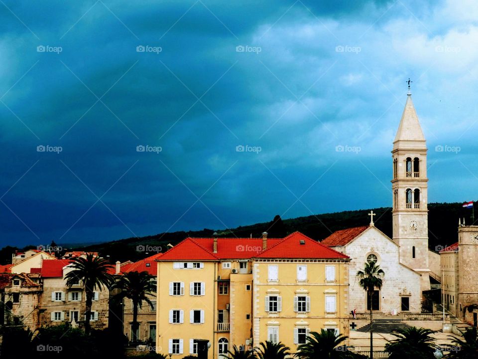 Pale coloured Venetian tower and red roofed yellow buildings against a dark stormy sky