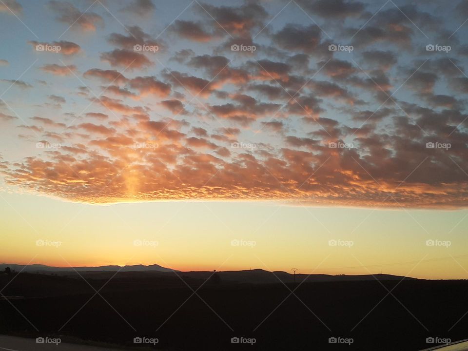 Scattered clouds add a touch of romance to the scene, while a lighthouse in the horizon completes a breathtaking natural artwork. This image is perfect for nature lovers.