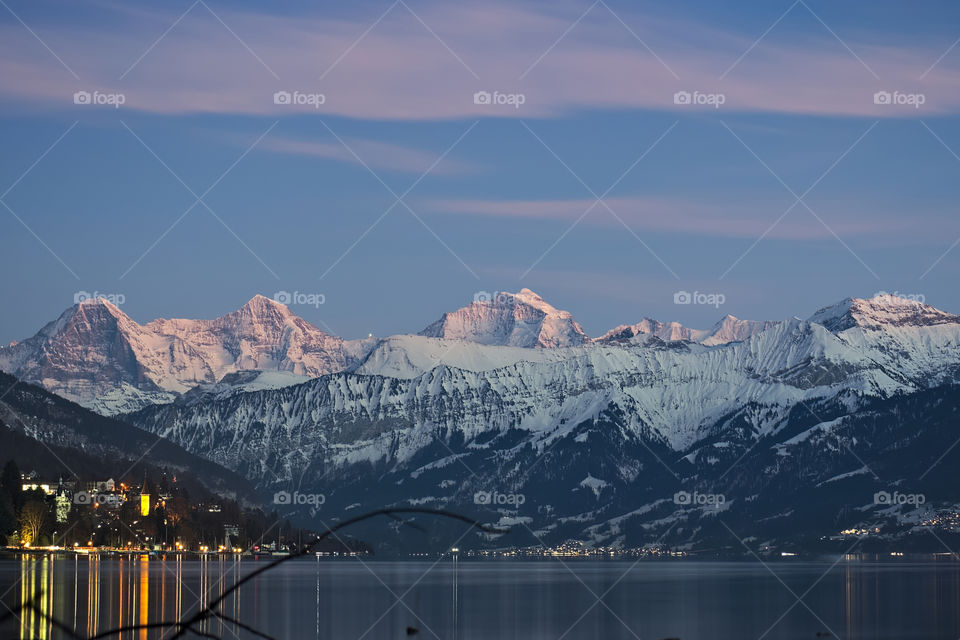 Winter snow mountains with little village lights reflected in lake thun.
