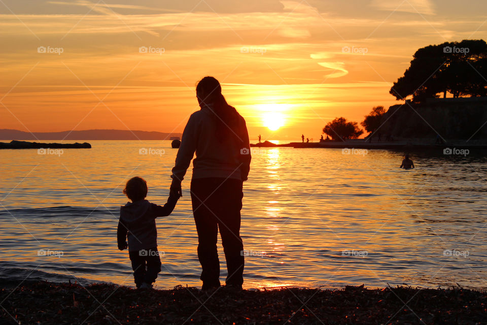 Silhouettes of mom and her little son on the beach at sunset