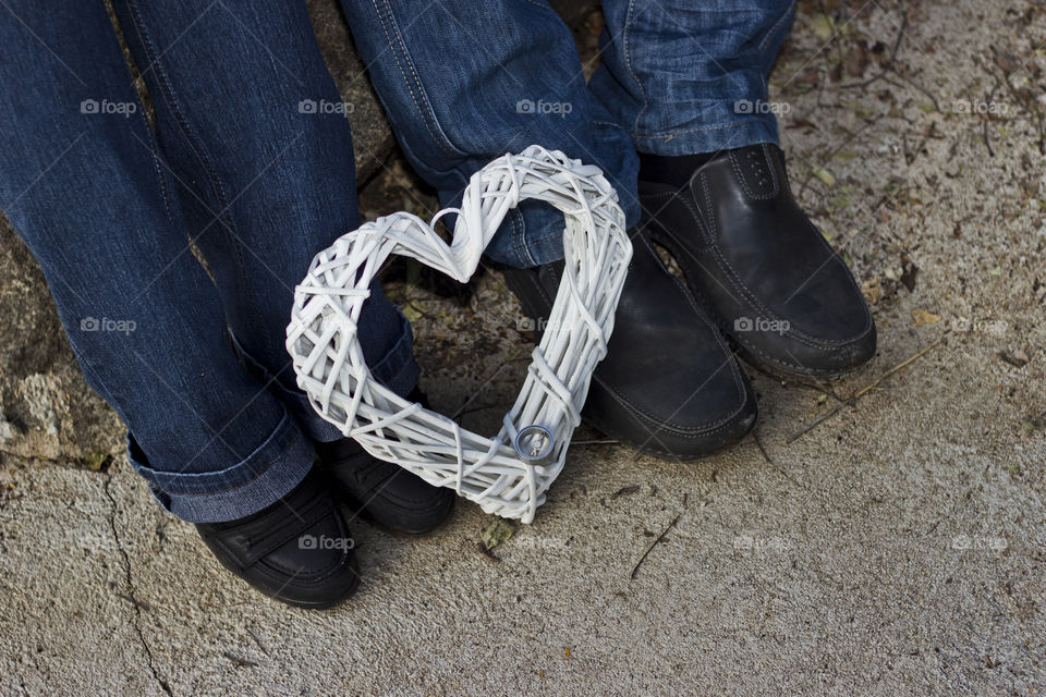 heart shape with wedding bands on it at peoples feet