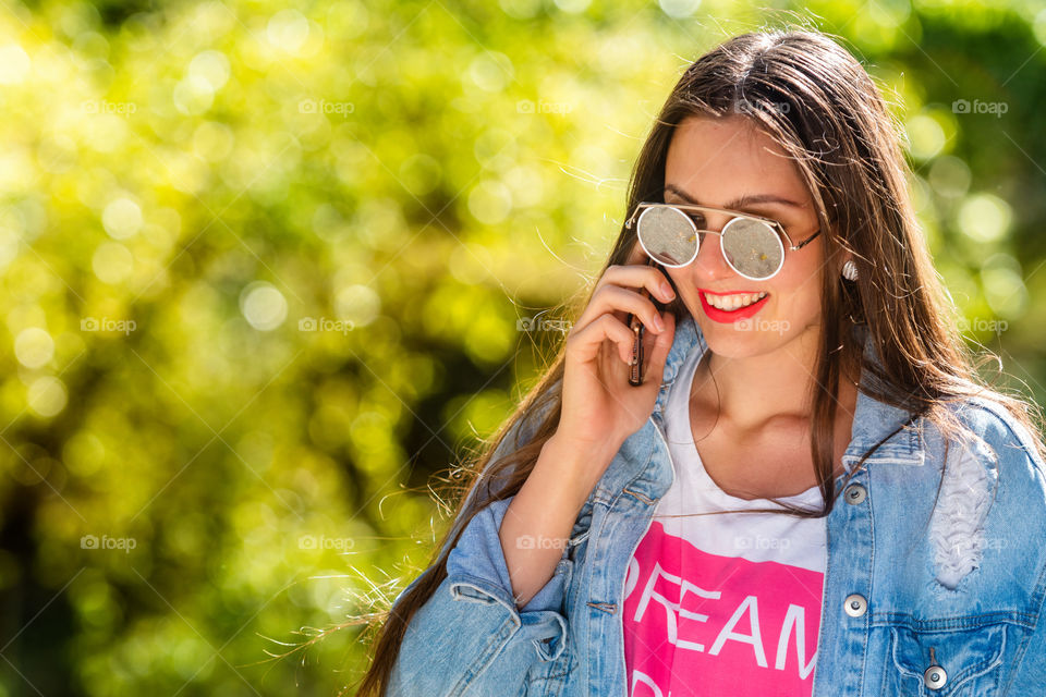 Beautiful, emotional, young woman in sunglasses talking on the phone. Copy space. Soft background.