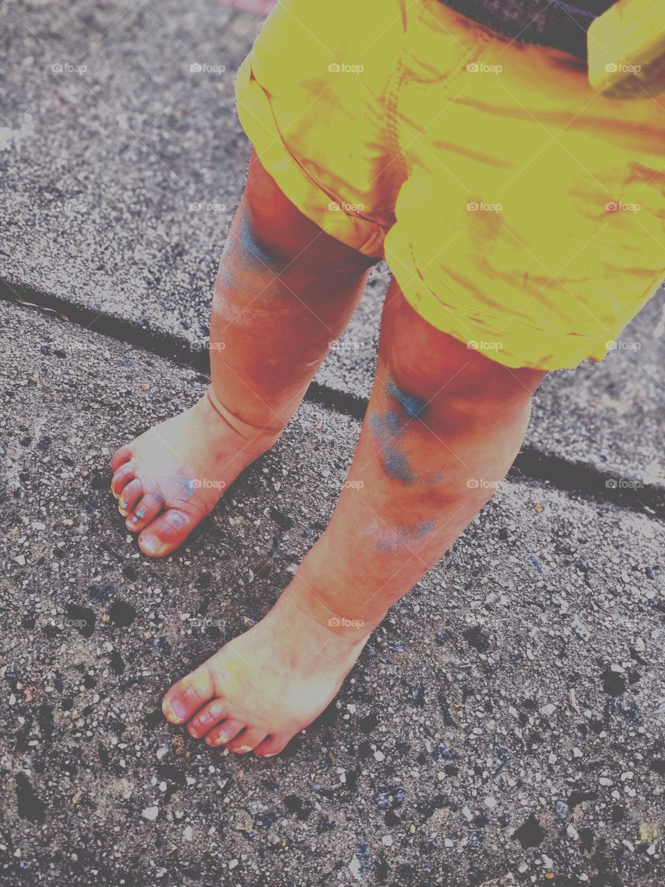 Toddlers feet, dirty with sidewalk chalk while coloring the driveway outside