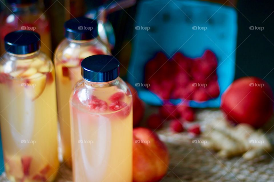 Kombucha, bottled for a second-ferment, flavored with nectarines, raspberries and ginger root slices on a natural fiber mat, whole nectarines and raspberries in a paper carton
