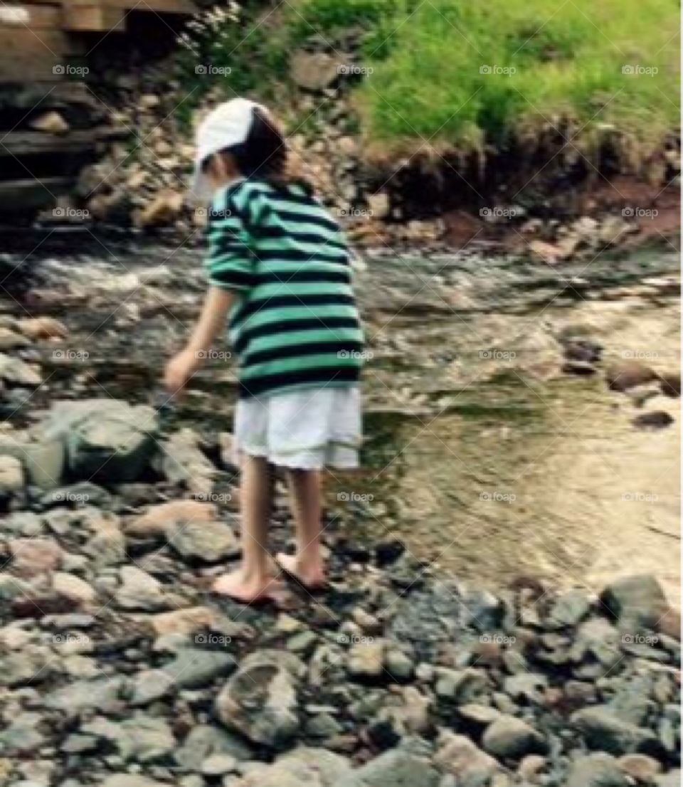 Little girl dipping toes on the river while hiking. Walking over rocks in the riverbed. 