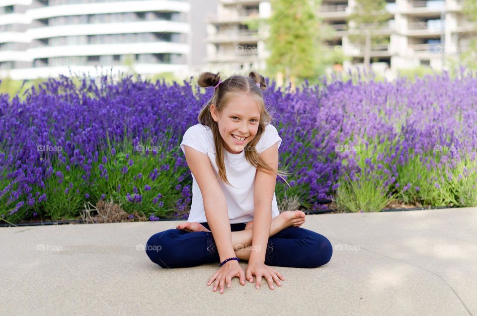 Little girl playing in city, park, doing yoga outdoor. Field of lavender flowers.  Having fun and laughing.