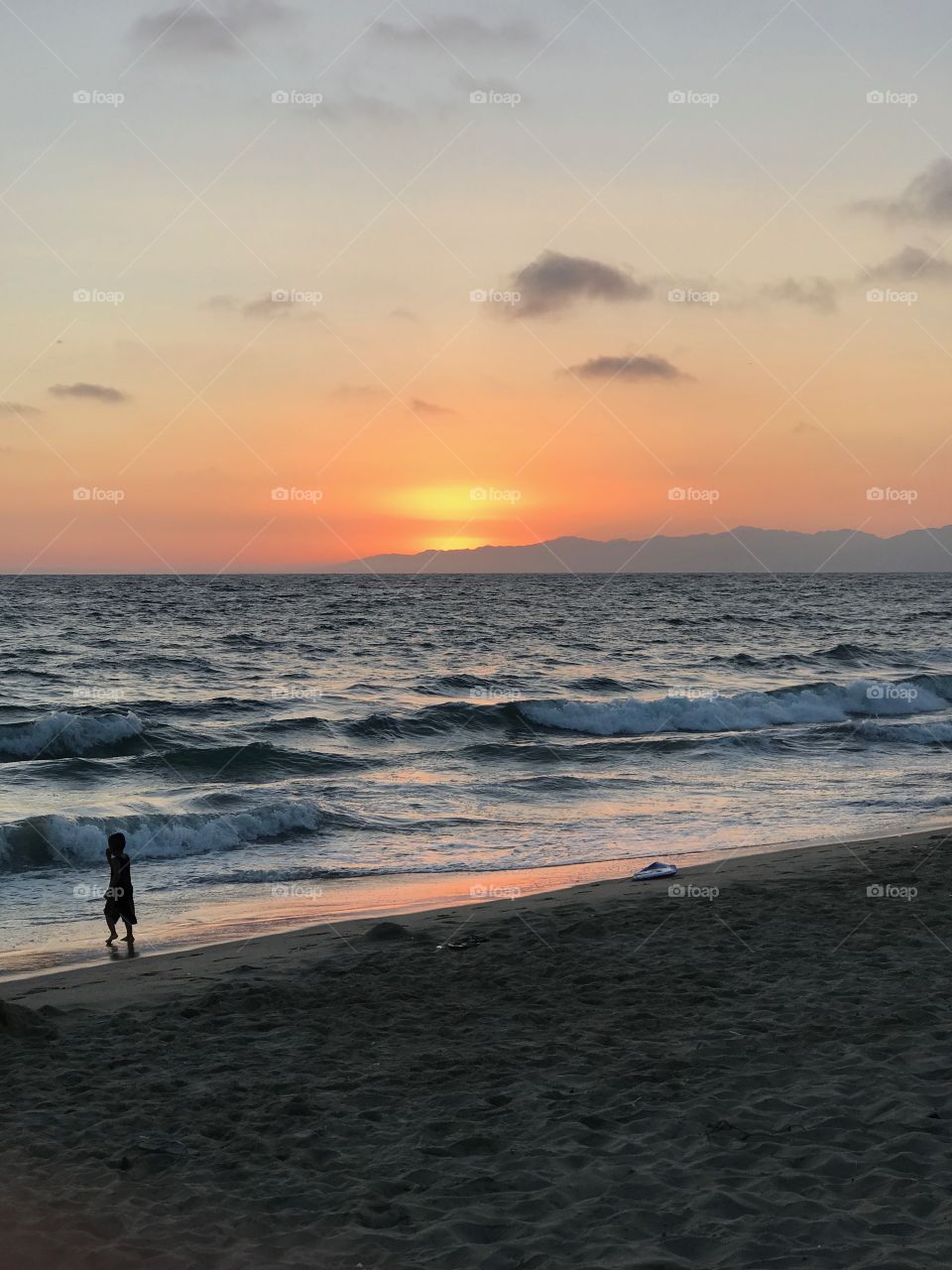 A view of the sunset over Dockweiler beach as a child walks across the sand 