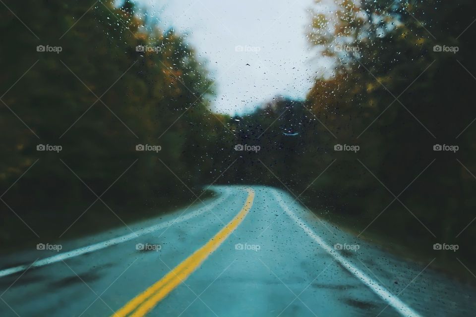 Raindrops on the windshield on a rainy day.

View of car windshield with rain drops as empty road in the background .