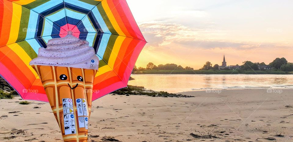 very cute icecream inflatable under rainbow colored sun umbrella at a river beach in The Netherlands at dawn