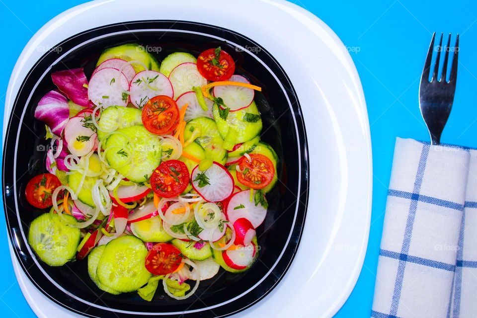 Fresh salad of radish,  cucumbers, leek, cherry tomatoes and dill in a black plate.  Top view of food