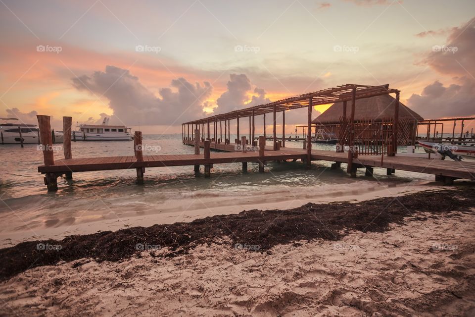 Wooden pier on the sea, the small port of Isla Mujeres shot with red light of the sunset over the sea.