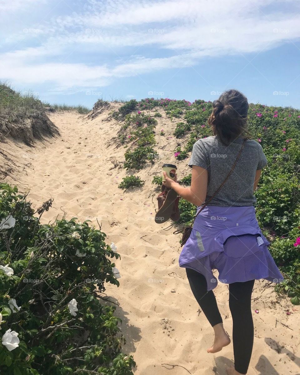 Woman walks over a sand bank to the beach.