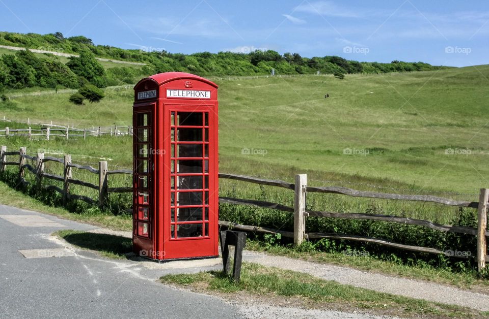 An old style red telephone box stands in contrast to the green field behind it