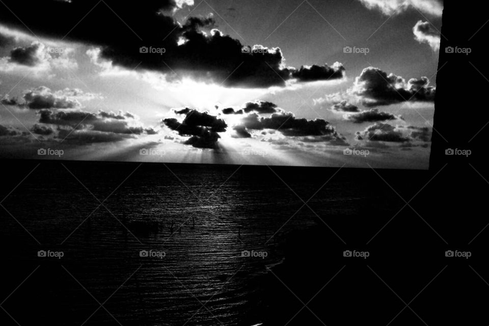 Black and white of a brilliant sunset on the beach of Cancun Mexico with backlit clouds and vivid sun rays. 