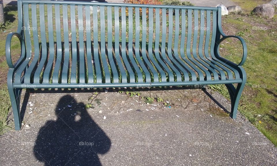 My shadow as I take a picture of this park bench.