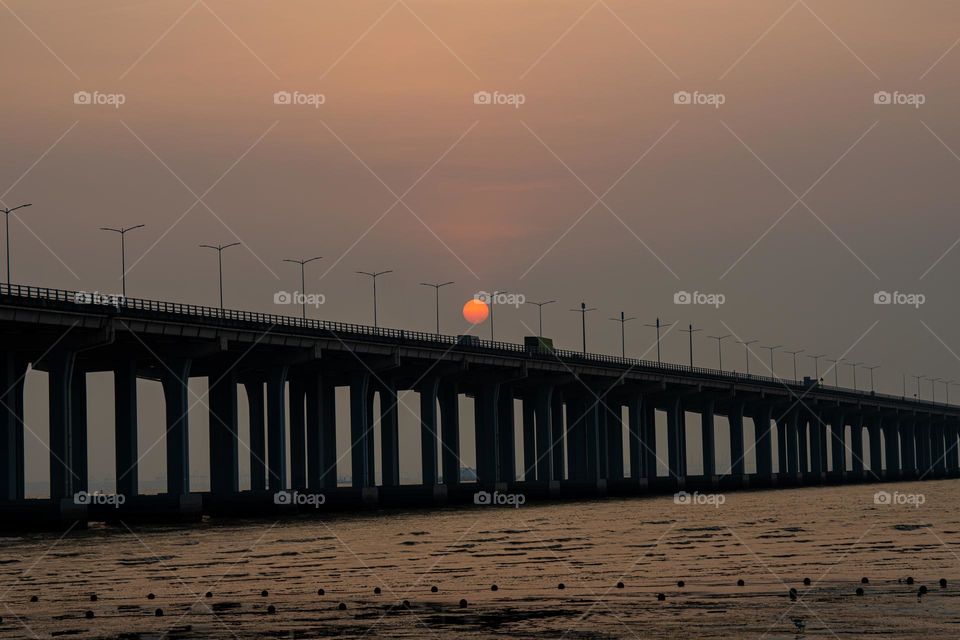 The view of sunset trapped between the poles of bridge.