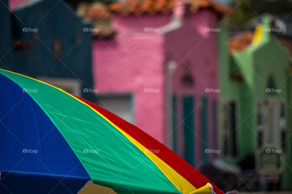Rainbow colored beach umbrella on a warm summer day with the colorful buildings of the Venetian in Capitola by the Sea in the background