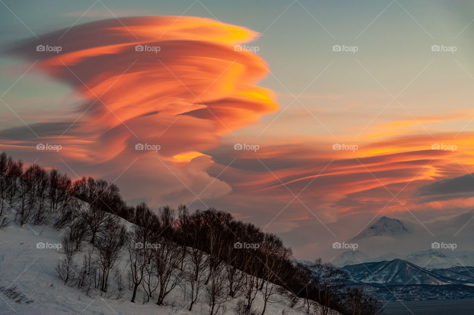 Kamchatka sunset, lenticular clouds rise on a snowy mountain, in the background you can see Vilyuchinsky volcano