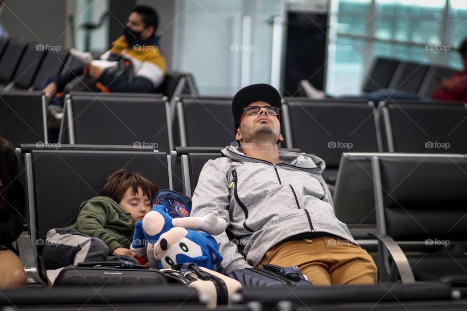 Man and a child are sleeping in chairs waiting for their flight at the airport