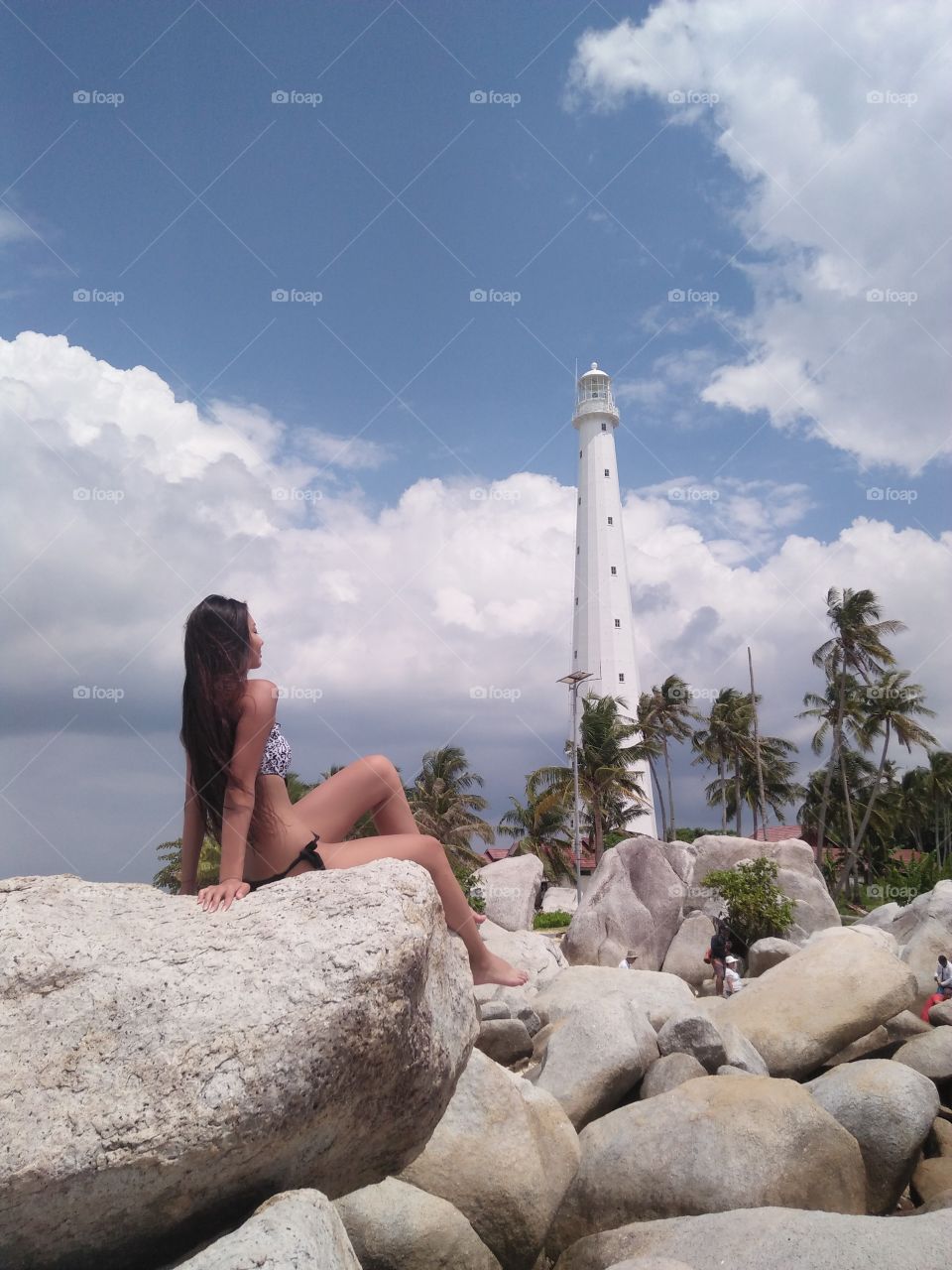 Woman in bikini posing on rock in front of lighthouse