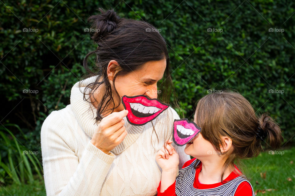 Smile! Mom and daughter having fun and laughing with oversized smiles made from paper