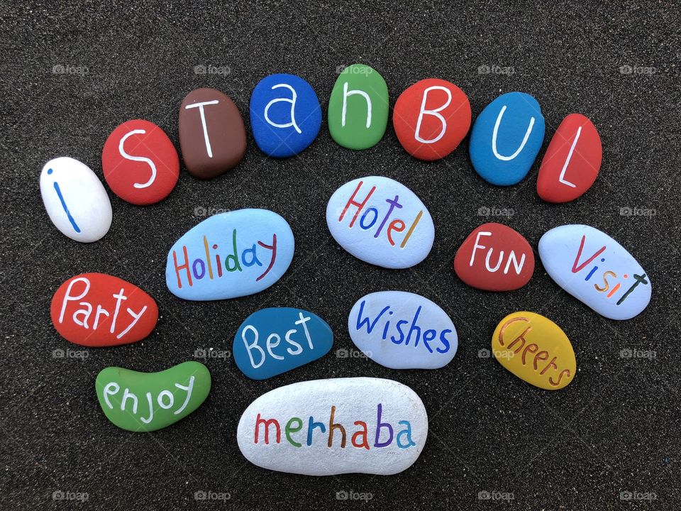 Visit Istanbul, cloud of words painted and carved on stones over black volcanic sand