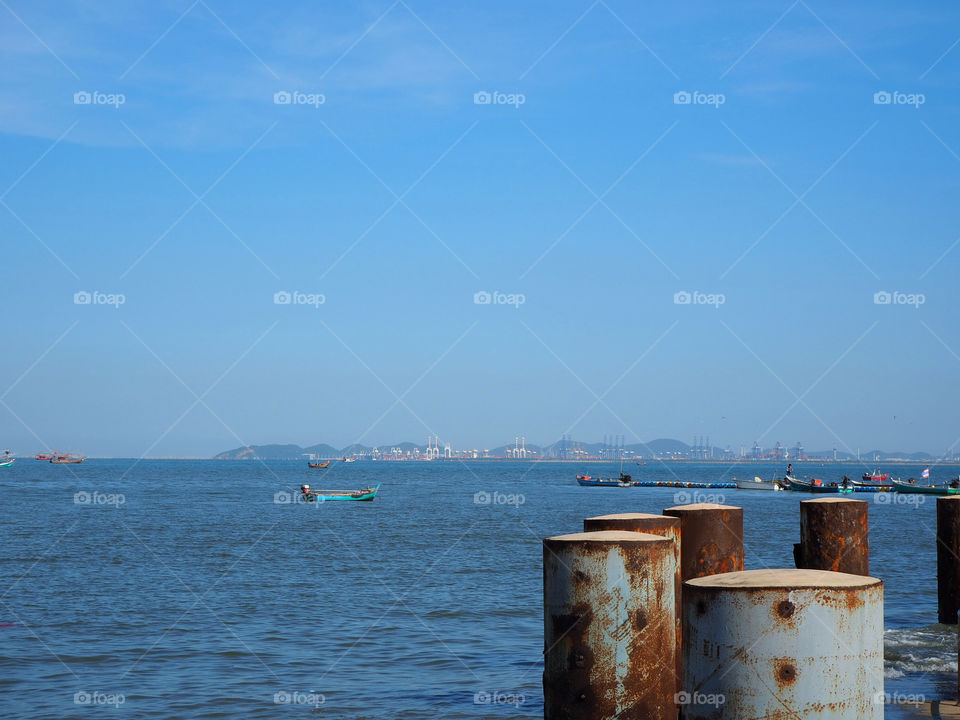 Harbor or pier with rusty metal pole and fishing boats and major seaport at the distant view.