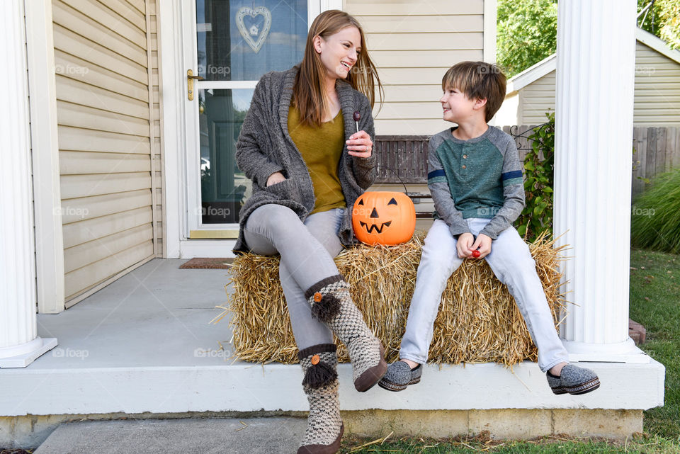 Mother and son sitting on a straw bale together with a jack o' lantern trick or treat bucket while eating candy