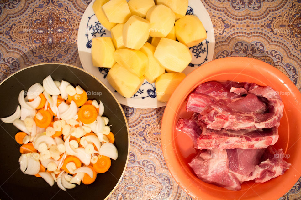 Meat, onions, carrots and potatoes in plate, frying pan and plastic container top view