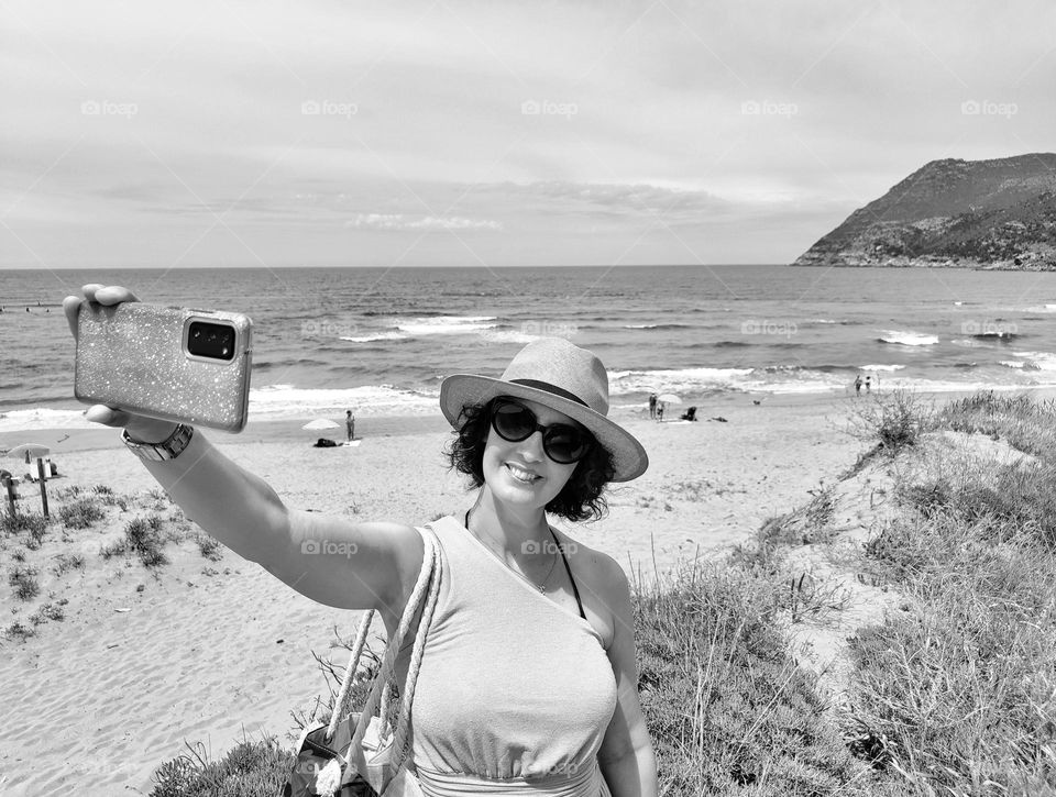 black and white photo of smiling woman making a selfie at the seaside