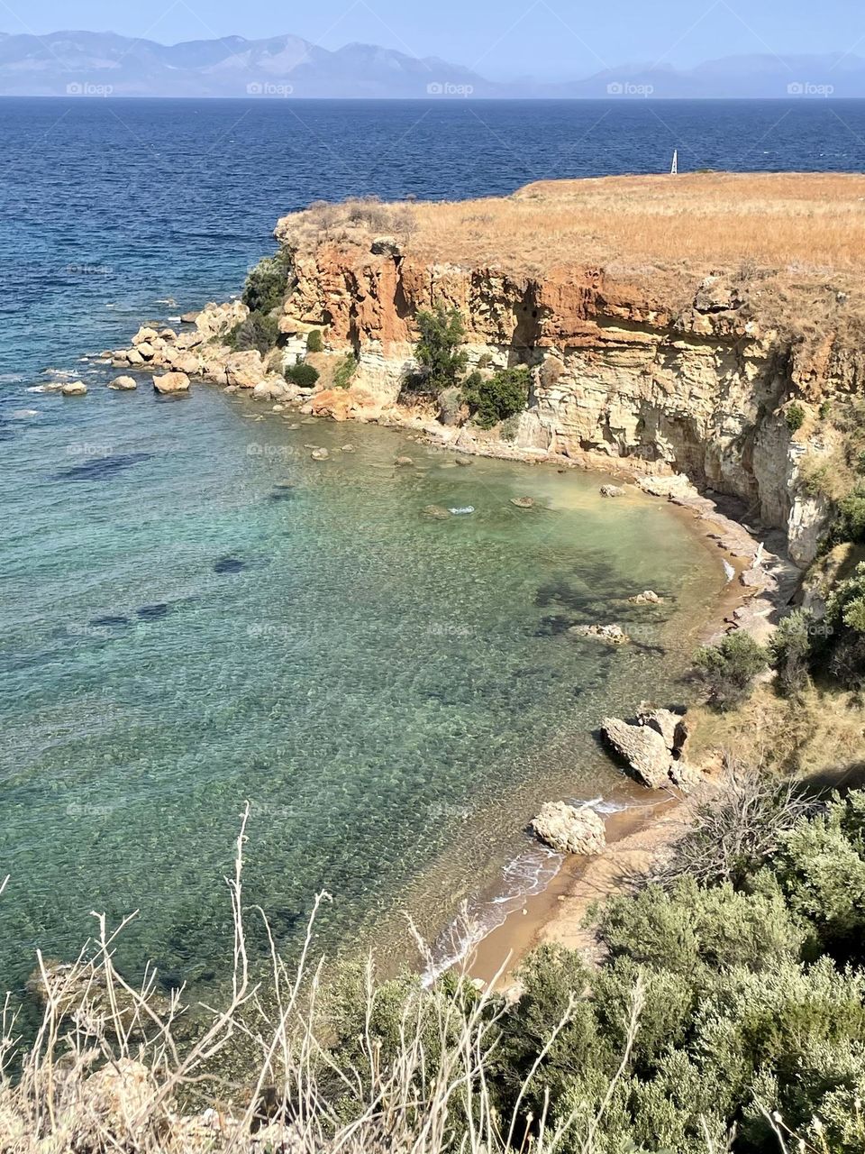 Turquoise-green waters shimmer beneath rocky hills by Koroni’s castle on a hot July day. The Messinian Gulf sparkles along Greece’s southern coast, with the distant Mani mountains rising beyond the sea.