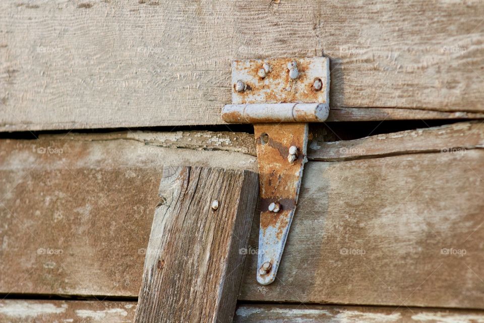 Closeup of a rusted hinge on a weathered wooden ventilation opening in the siding of an antique farm building  