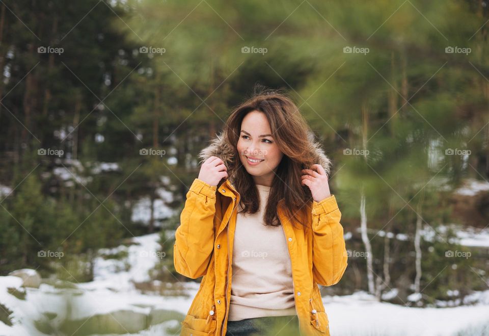 Portrait of young smiling beautiful woman in yellow jacket walking in the winter forest