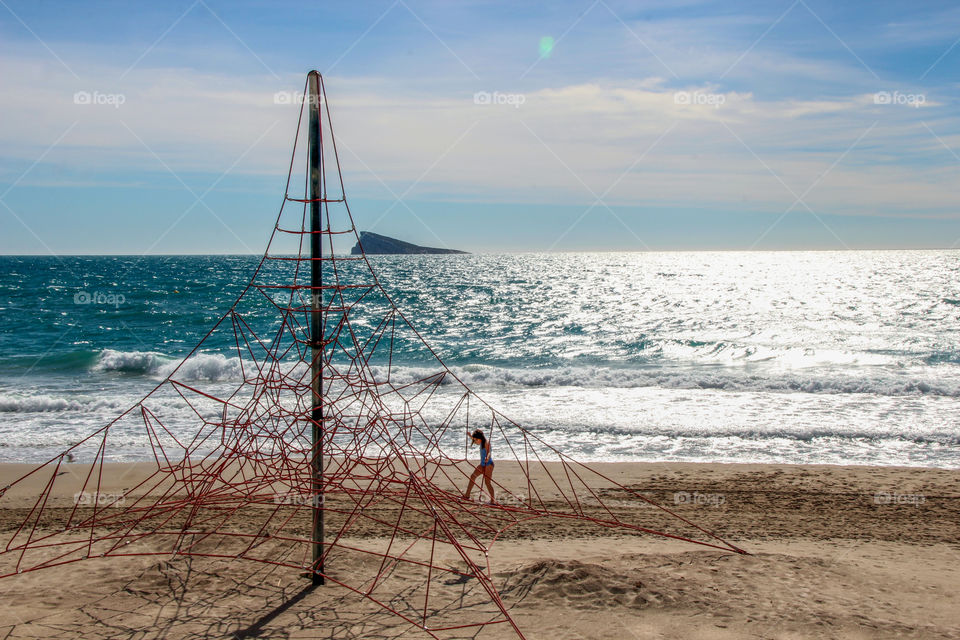 Young girl exploring the climbing net on an Alicante beach