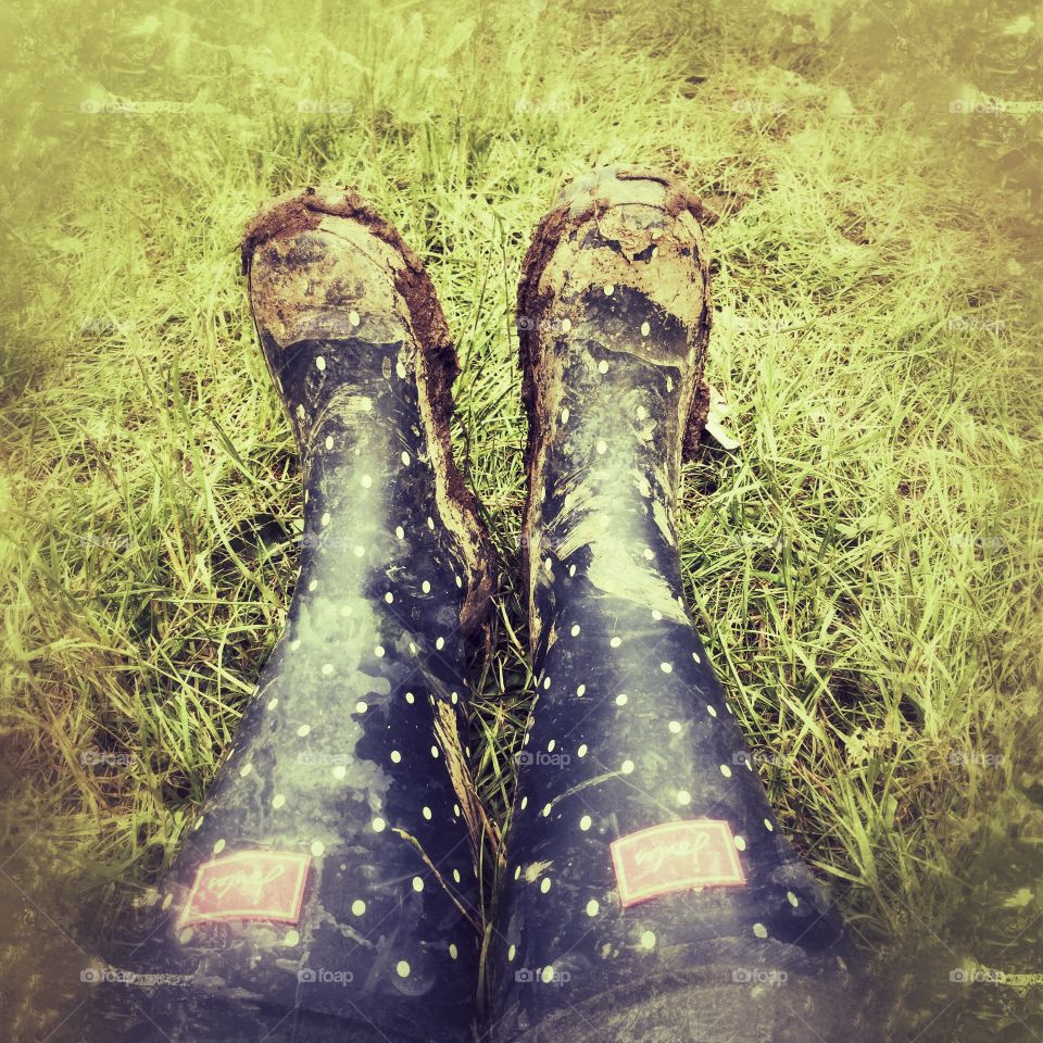 Woman’s feet in muddy wellies sitting in a field 