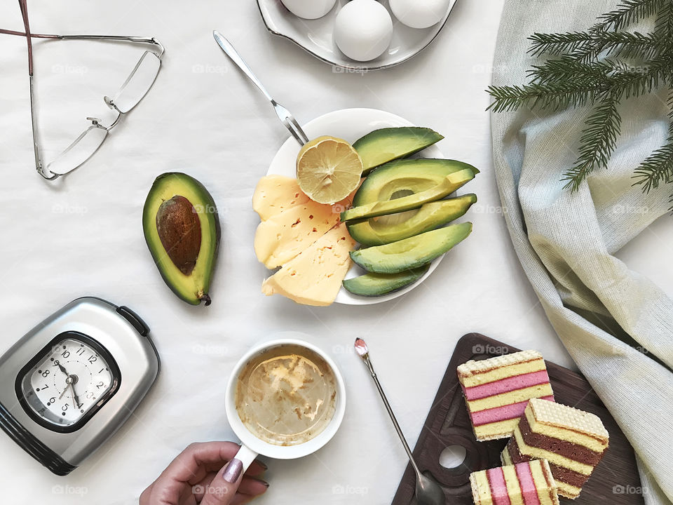 Overhead view of a favorite breakfast - boiled eggs, cheese, avocado, cookies and cup of coffee with milk 