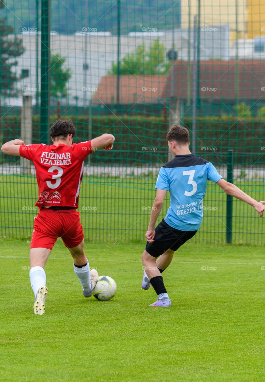 Two teenagers wearing club jerseys chasing a ball at an official football match