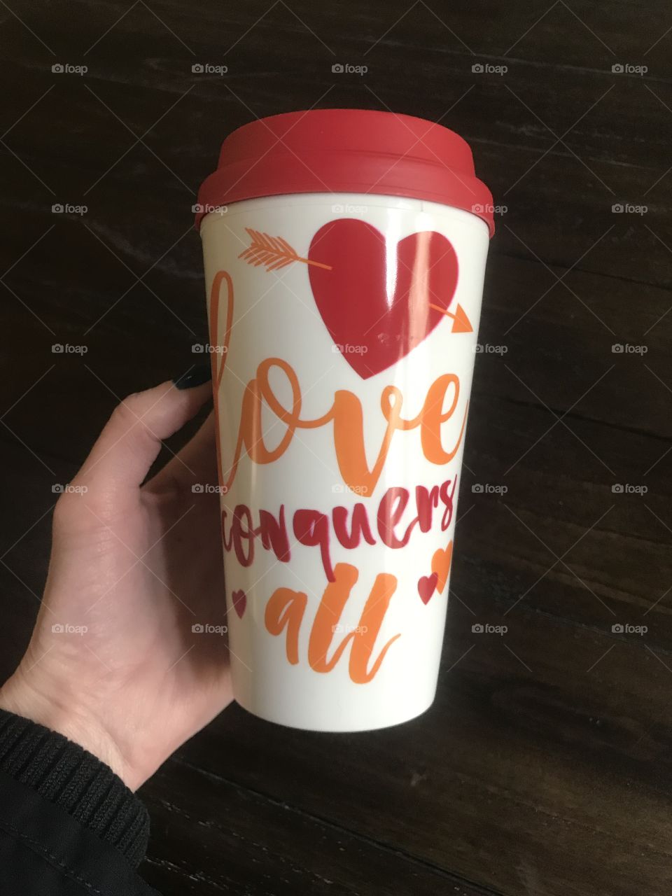 A lady holding a Valentines coffee mug saying loves conquers all with red hearts and arrows. USA, America 