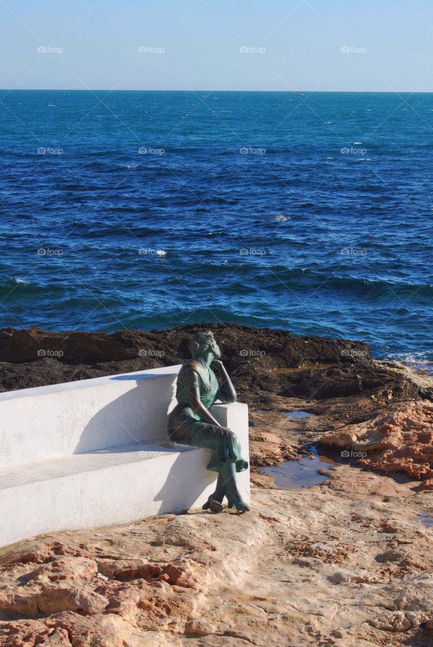 Statue of a Girl sitting alone watching the sea