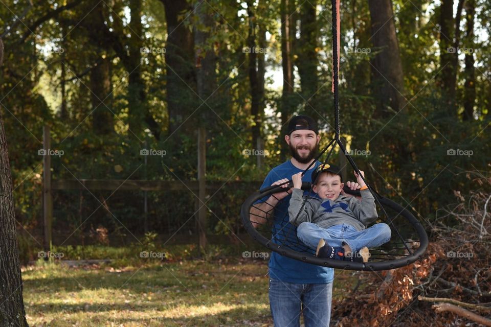 A dad abs son playing on a tree swing in the back yard 