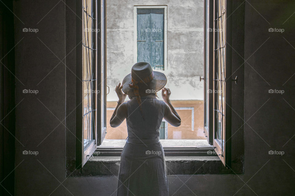 Woman wearing a dress and a hat looking out of the window.