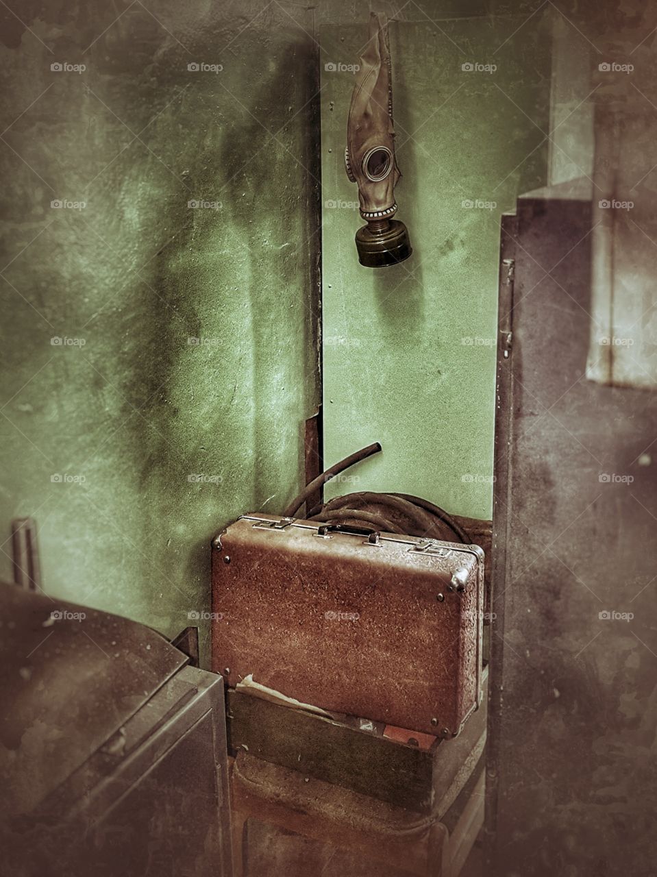 A gas mask weighs over an old suitcase in a room without windows.