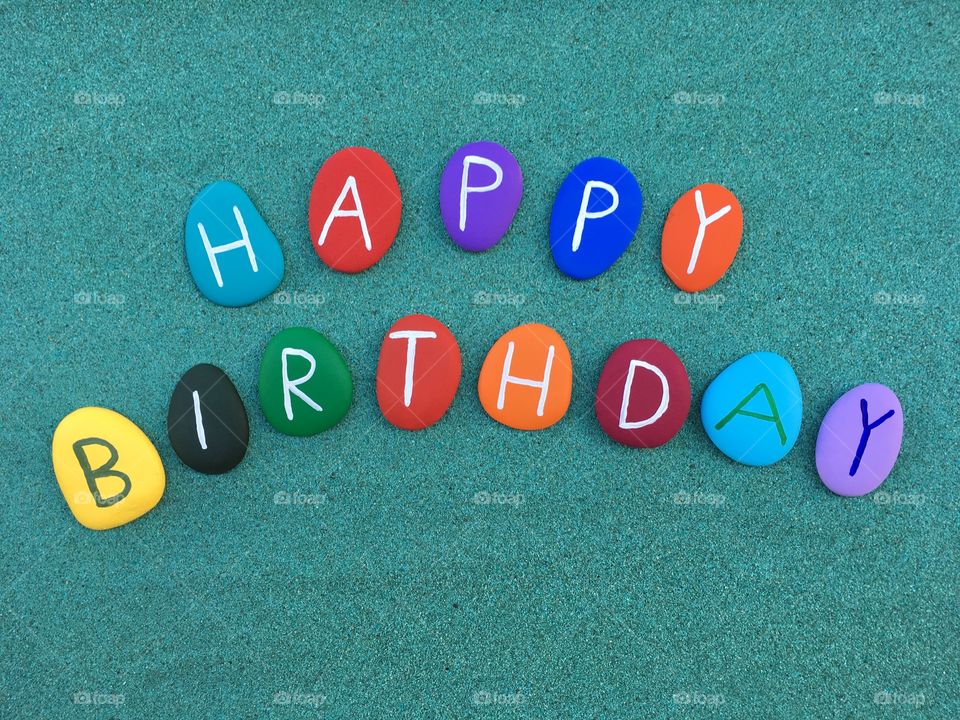 Happy Birthday on colored stone letters over green sand 
