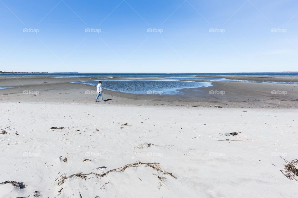 Finding a place of your own, one man walking alone on a wide sand beach by the ocean 