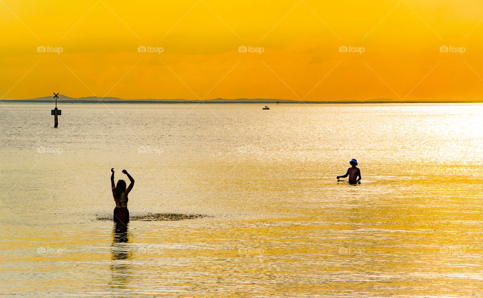 golden skies over Melbourne beach at sunset with silhouettes of two people enjoying the warmth of the sea